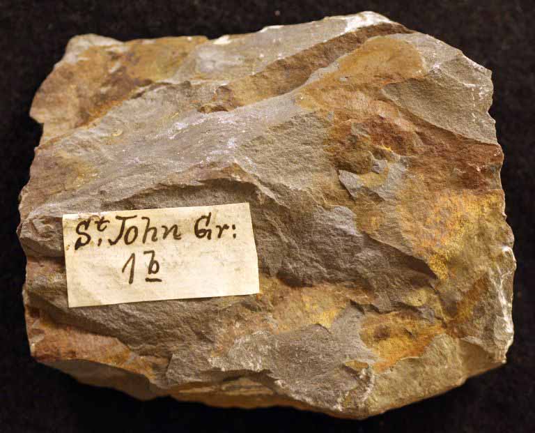 Colour image of brown rock with orange streaks and paper label