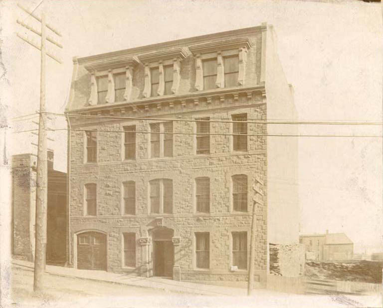 Photographie noir et blanc d’un ancien bâtiment de quatre étages avec des fenêtres donnant sur la rue