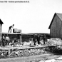 Black and white photograph of rock mine, buildings, sheds, rocks and man on roof of shed