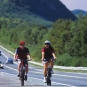 Colour photograph of two cyclists, highway and mountain in background