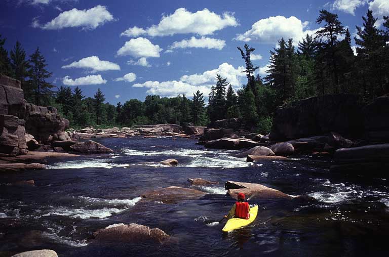 Photographie couleur montrant une personne en kayak jaune dans des rapides