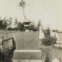 Photographie noir et blanc d’une pierre tombale carrée surmontée d’une urne en pierre dans un cimetière