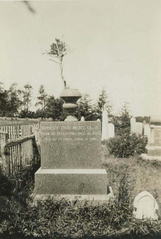 Black and white photograph of a square headstone in a cemetery with a stone pot on top