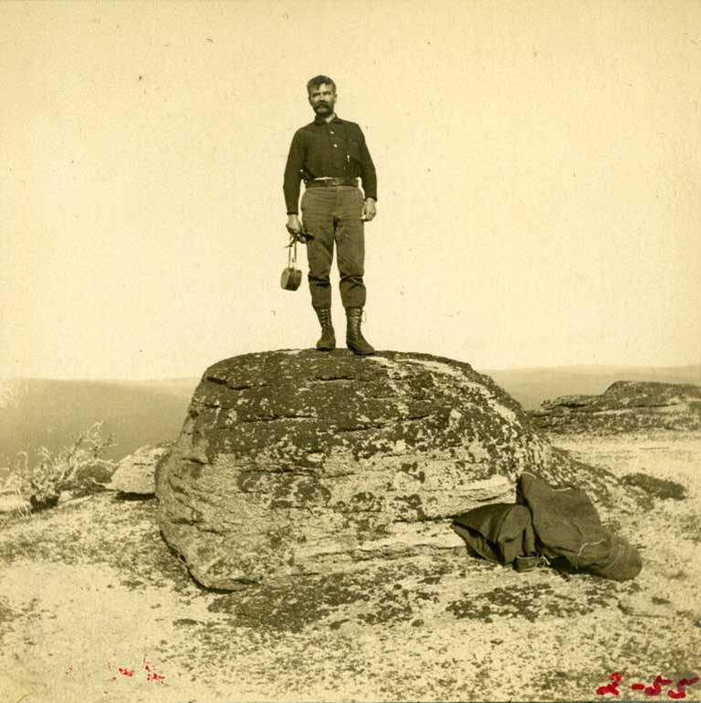 Black and white photograph of man standing on a large boulder