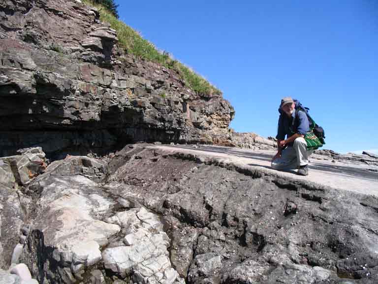 Colour photograph of a man in front of a cliff kneeling on the rock